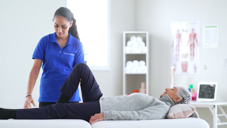 A young female Physiotherapist of Middle Eastern decent, has a senior patient lay on her table as she puts her through a series of stretches to asses her injury. The therapist is dressed professionally as she works the seniors leg through different movements to asses her rage of motion.